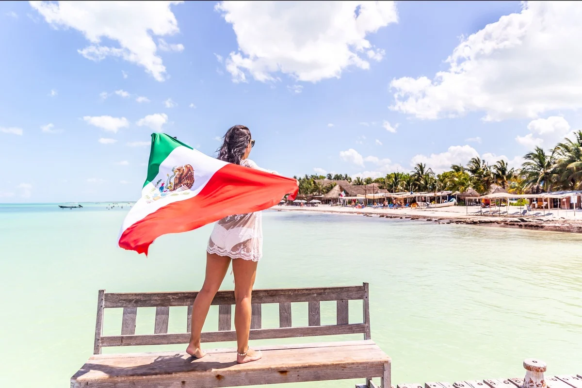 Young Female Tourist Flying The Mexican Flag As She Stares At The Ocean